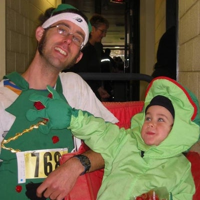 A man dressed up as a christmas tree and a boy sitting down dressed up as a frog