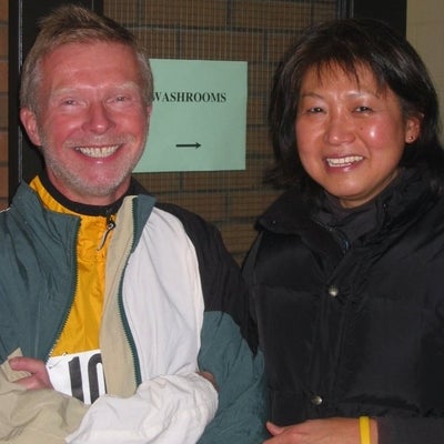 A man and woman smiling towards the camera in front of washrooms sign