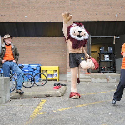 A man watching while a lion mascot and a woman with a megaphone leading a warm up before the race
