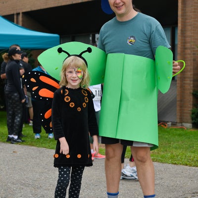 Young girl dressed as a butterfly standing next to a man dressed as a flower.