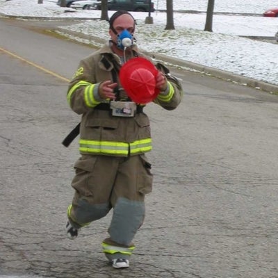 A male dressed as a firefighter running down the road. 