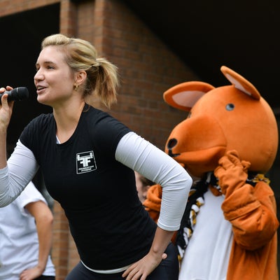 Woman singing into a microphone with kangaroo mascot in the background.