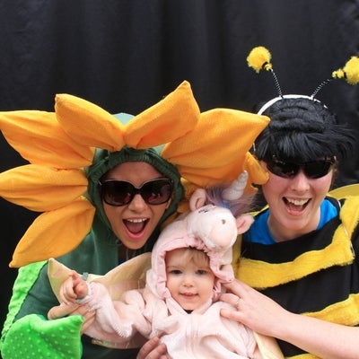 Two ladies dressed up as a flower and bee holding a baby in a costume.