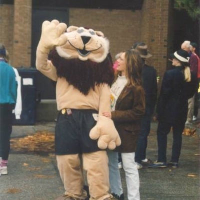 A woman standing with a lion mascot.