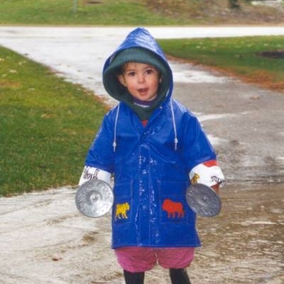 A liitle boy with blue raincoat and rain boots holding two large cloth buttons