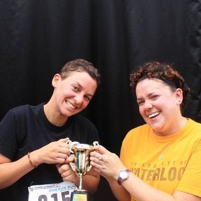 Two ladies smiling and holding a little trophy together.