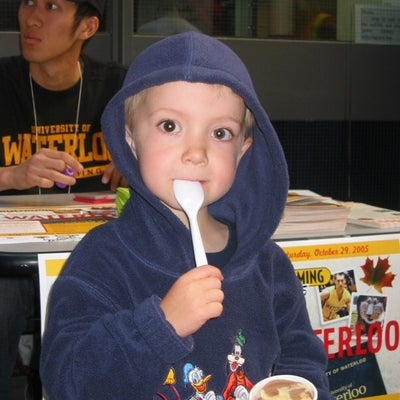 A boy holding a spoon and a cup of ice cream 