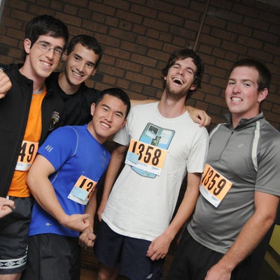 Five runners similing towards a camera inside of Applied Health Sciences building after the race