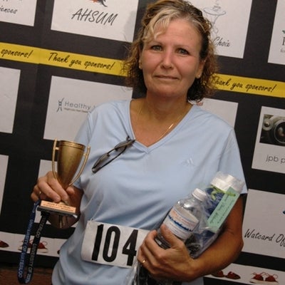 Female holding a trophy and two water bottles in front of the AHS Fun Run and other bulletin board