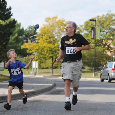 A man and a boy running together while the boy is trying to catch a flying object