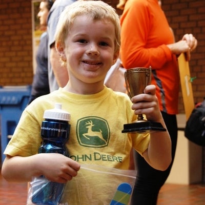 A child holding his trophy with his left hand while holding a water bottle and a plastic bag with his right hand