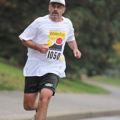 A man wearing University of Waterloo t-shirt and a white cap running