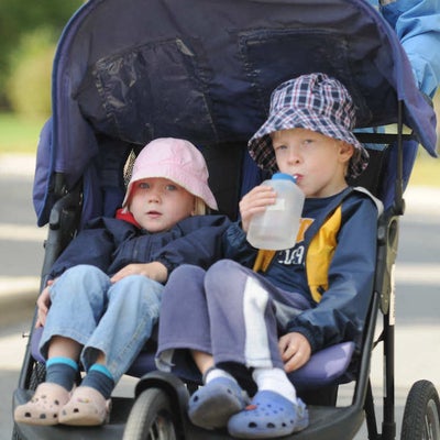 Two little kids in one baby stroller while one of them drinking water