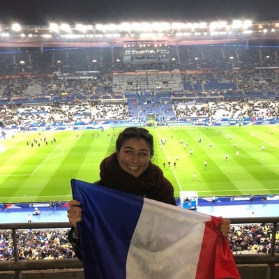 Aysun holding up a French national flag in front of a stadium.