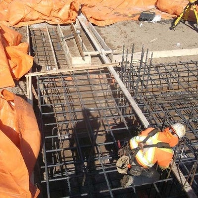 Construction workers placing rebar and framework for north footing of expansion building.
