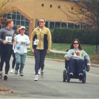 Four runners walking down the road with a female participant on a wheel chair