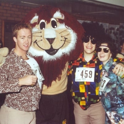 A lion mascot with three male participants 