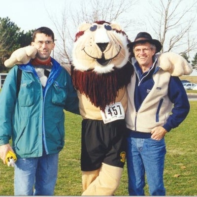Two men standing with a lion mascot in the middle
