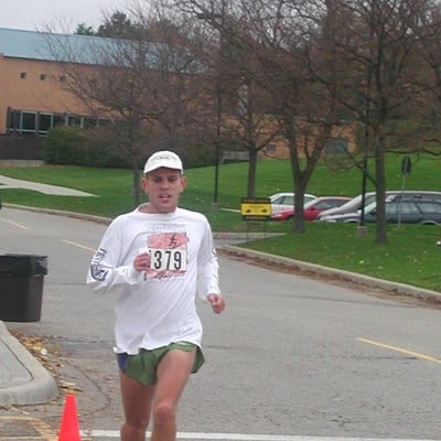 A male runner with a white cap on running down the road.