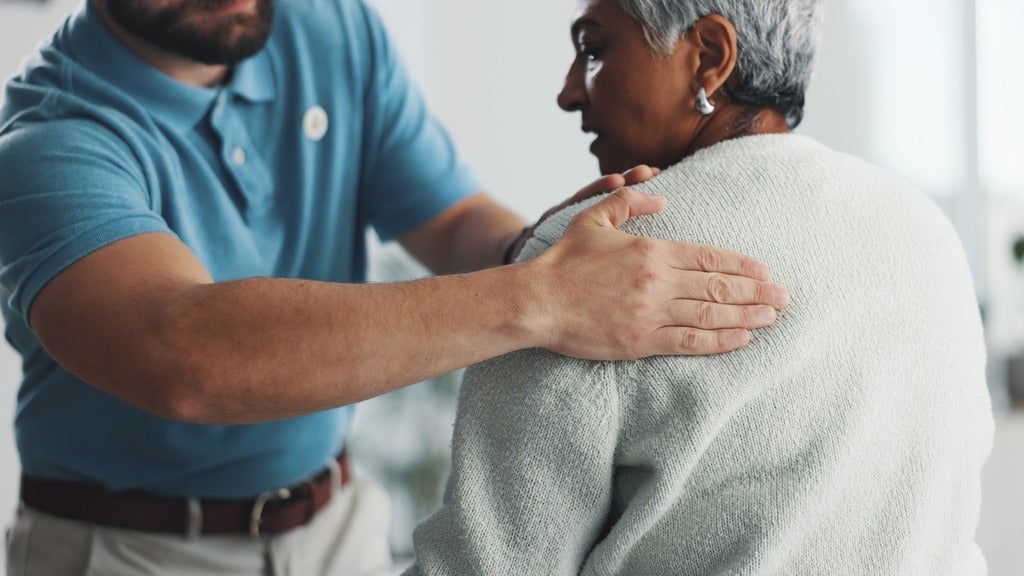 Physiotherapist touches older woman's shoulder.