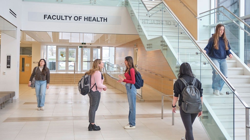 Students talking and walking through Health building on campus.