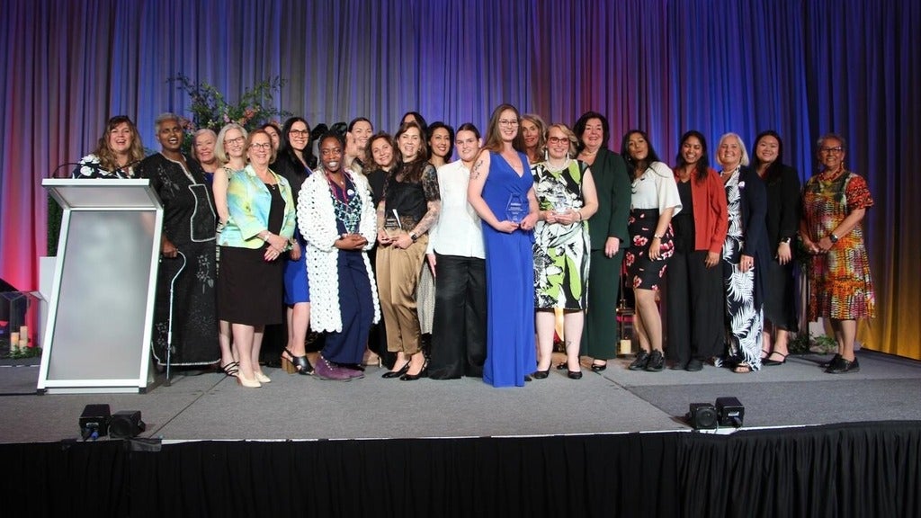 24 winners and nominees stand on stage smiling.