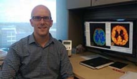 Andrew sitting at his office desk in front of computer displays showing brain image