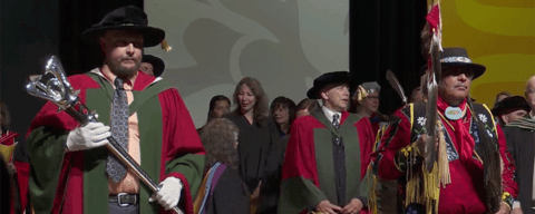 Dr. Leatherdale carries convocation mace beside Elder Henry carrying the Eagle Staff. 