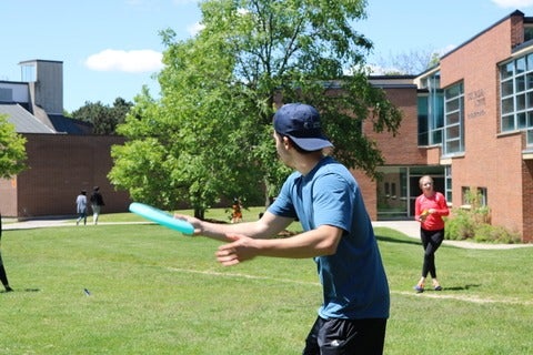Student throws a frisbee on the green area behind the BMH building on campus.
