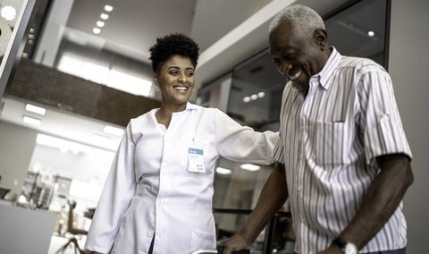 Health care professional assists an elderly patient with walking.