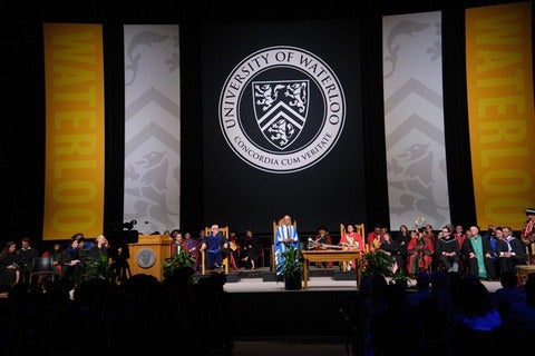 University president and faculty members on spotlit convocation stage.