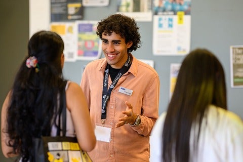 Smiling person with lanyard and nametag talks to students at booth.