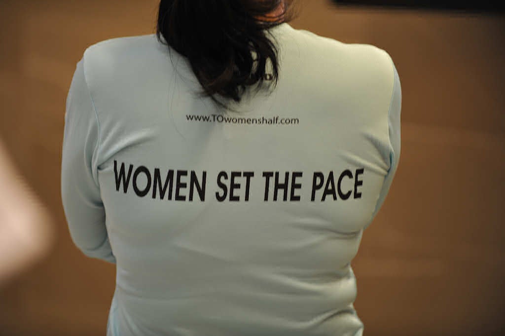 Close shot of woman wearing a shirt written "Women set the pace" on the back 