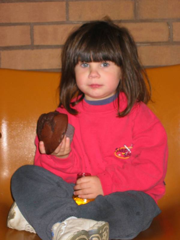 A girl sitting down on a chair holding a brownie and a bottle of juice 