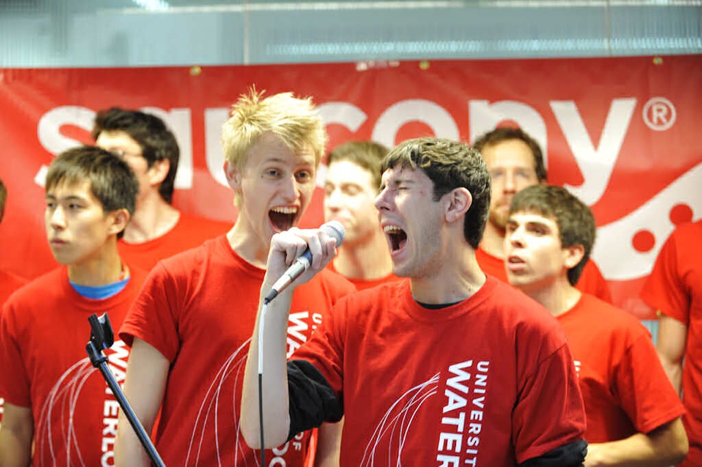 Two males singing with a microphone among other people