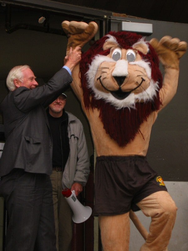 Man wearing a suit holding a lion mascot's hand