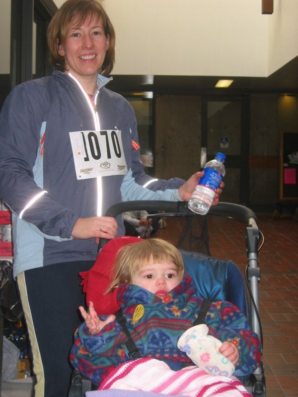A woman holding a water bottle stadning beside her baby in a baby stroller 