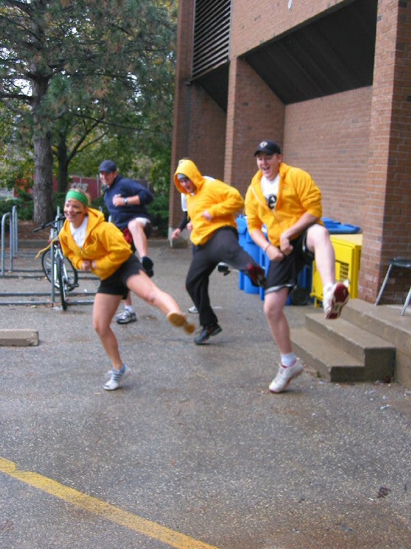Three students in yellow hoodies and one in a blue sweater doing a dance move 