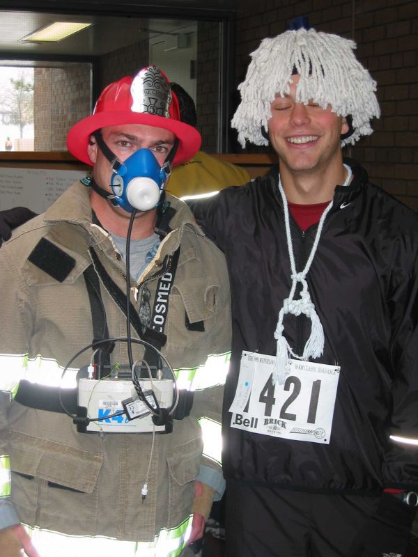 Man dressed as a firefighter with friend having a mop on top of his head smiling
