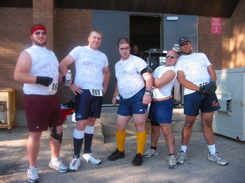 Five male runners with numbers written on their shirts posing 