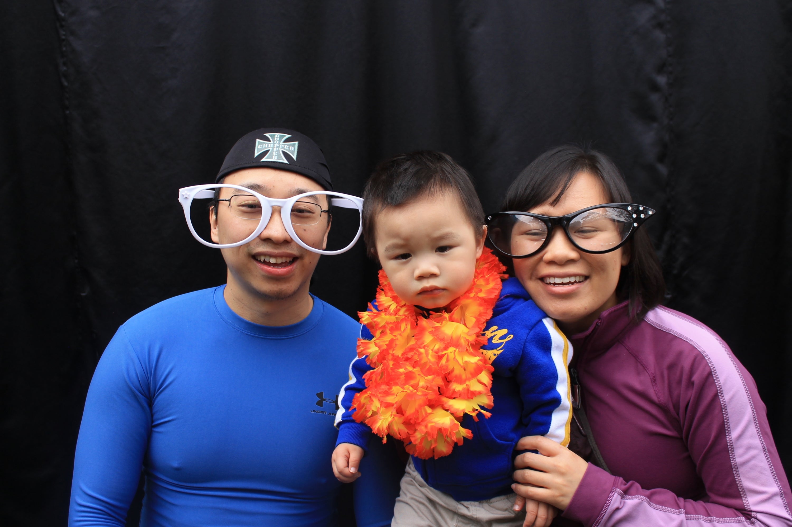 A man and woman wearing funny large glasses with a baby wearing a boa scarf.