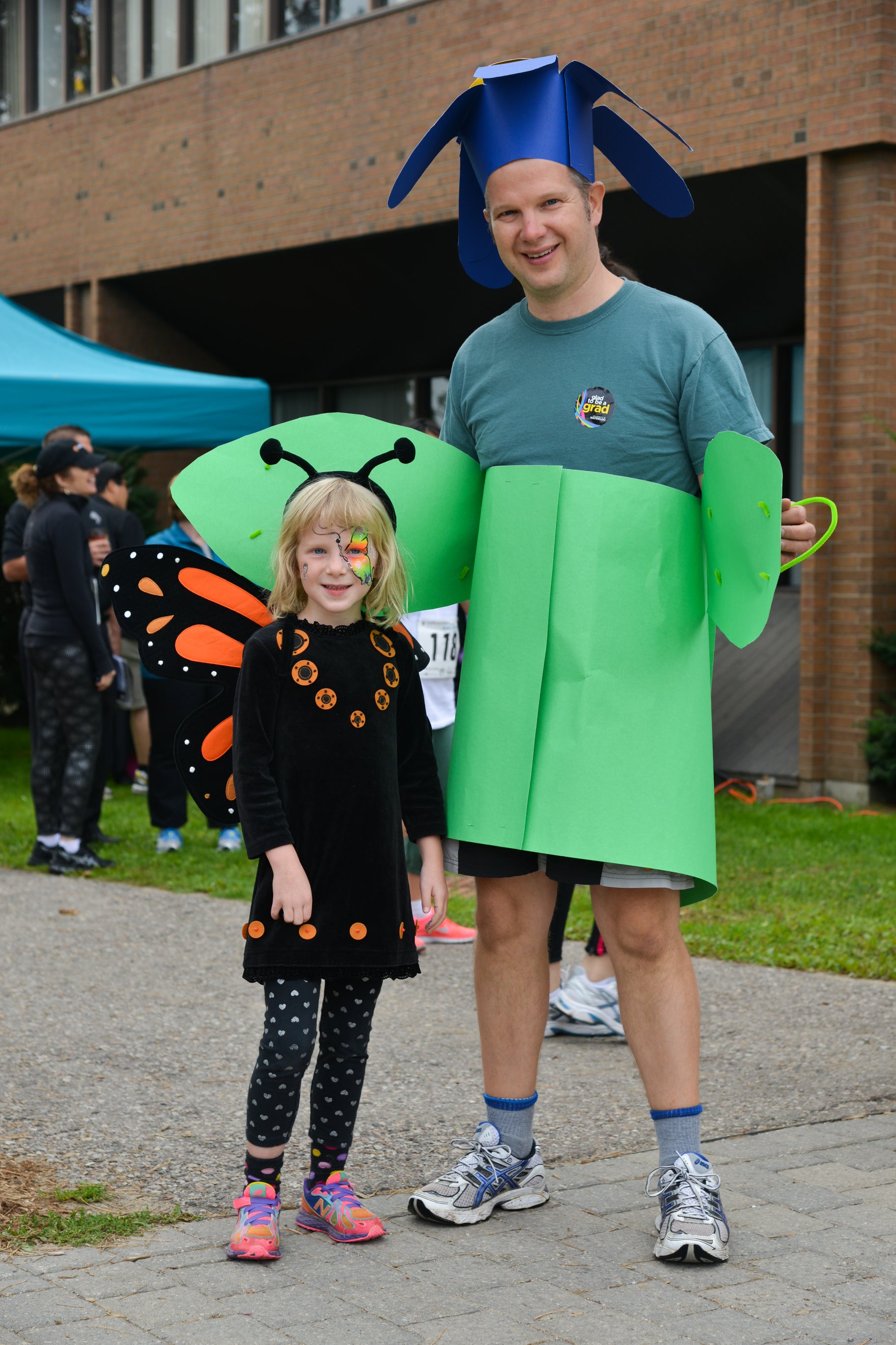 Young girl dressed as a butterfly standing next to a man dressed as a flower.