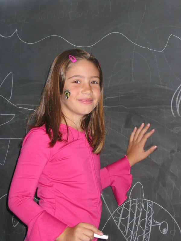 A girl in a pink shirt drawing on a chalkboard