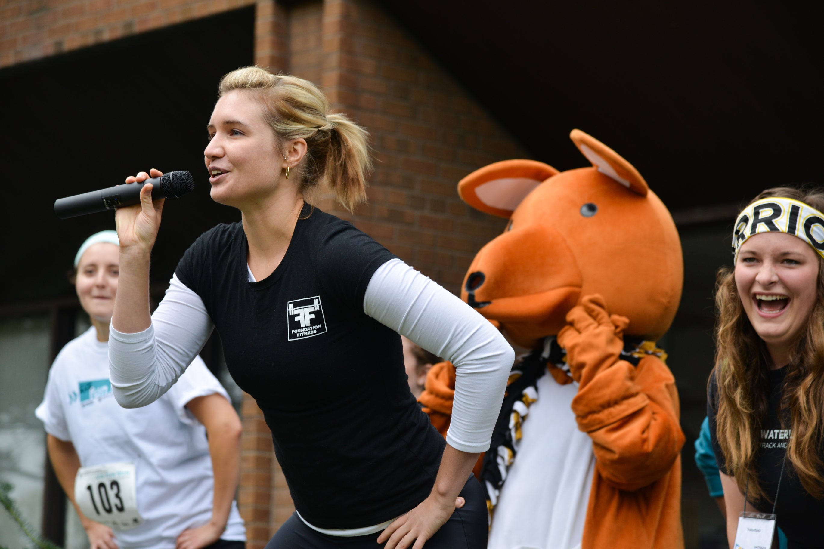 Woman singing into a microphone with kangaroo mascot in the background.