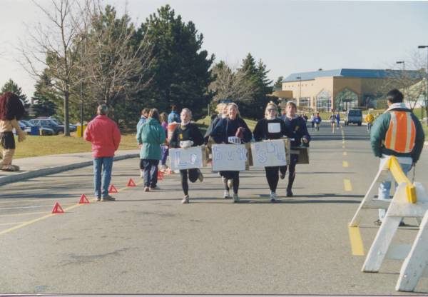 Six individuals jogging with signs strapped to their waist 