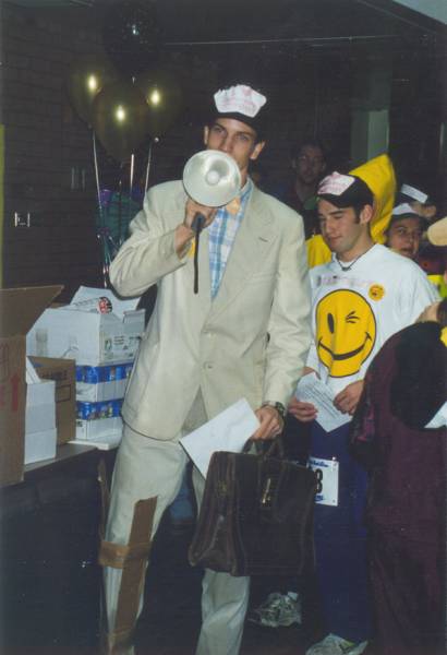 A man in a beige suit talking through a megaphone among people.