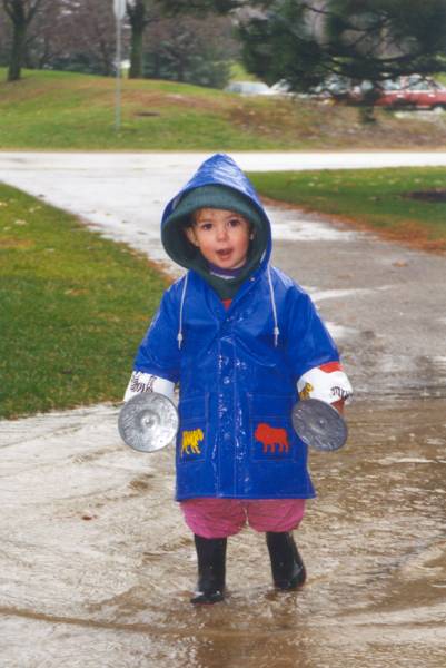 A liitle boy with blue raincoat and rain boots holding two large cloth buttons