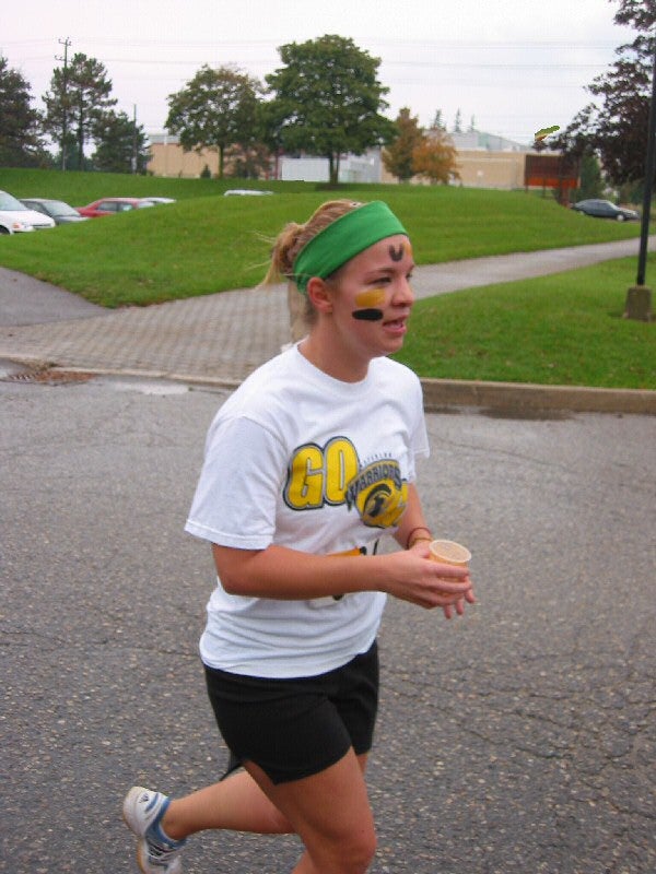 A female runner with face painting on her face running while holding a cup of water