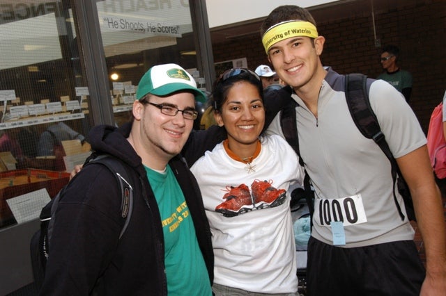 Two male runners and a female runner smiling towards a camera