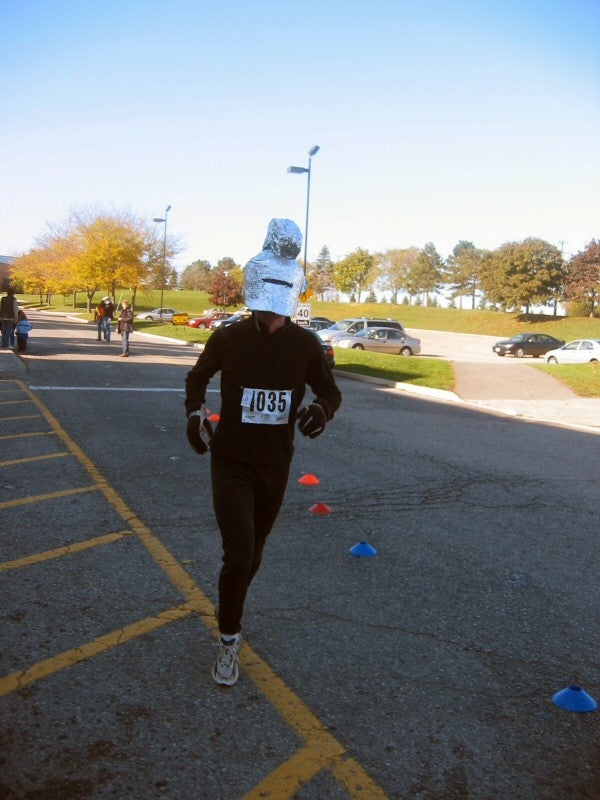 A man running in a track suit with alumini foil made roman helmet on his head